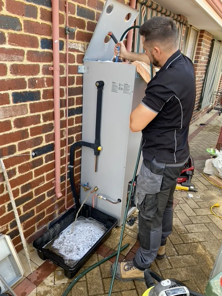 A Sureflow plumber fitting a hot water system against a brick wall
